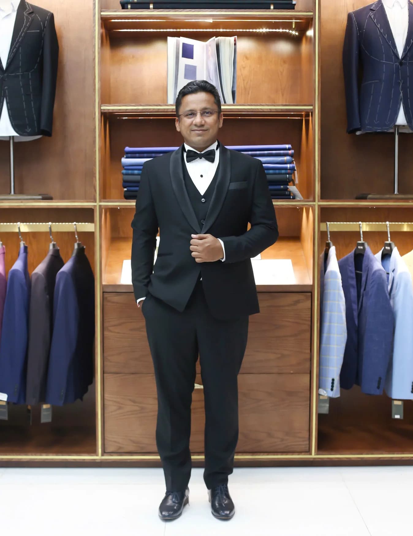 Quý ông tuxedo đen ba mảnh, nơ đen trong showroom gỗ sang trọng, vest nam may đo tại Đường 3/2