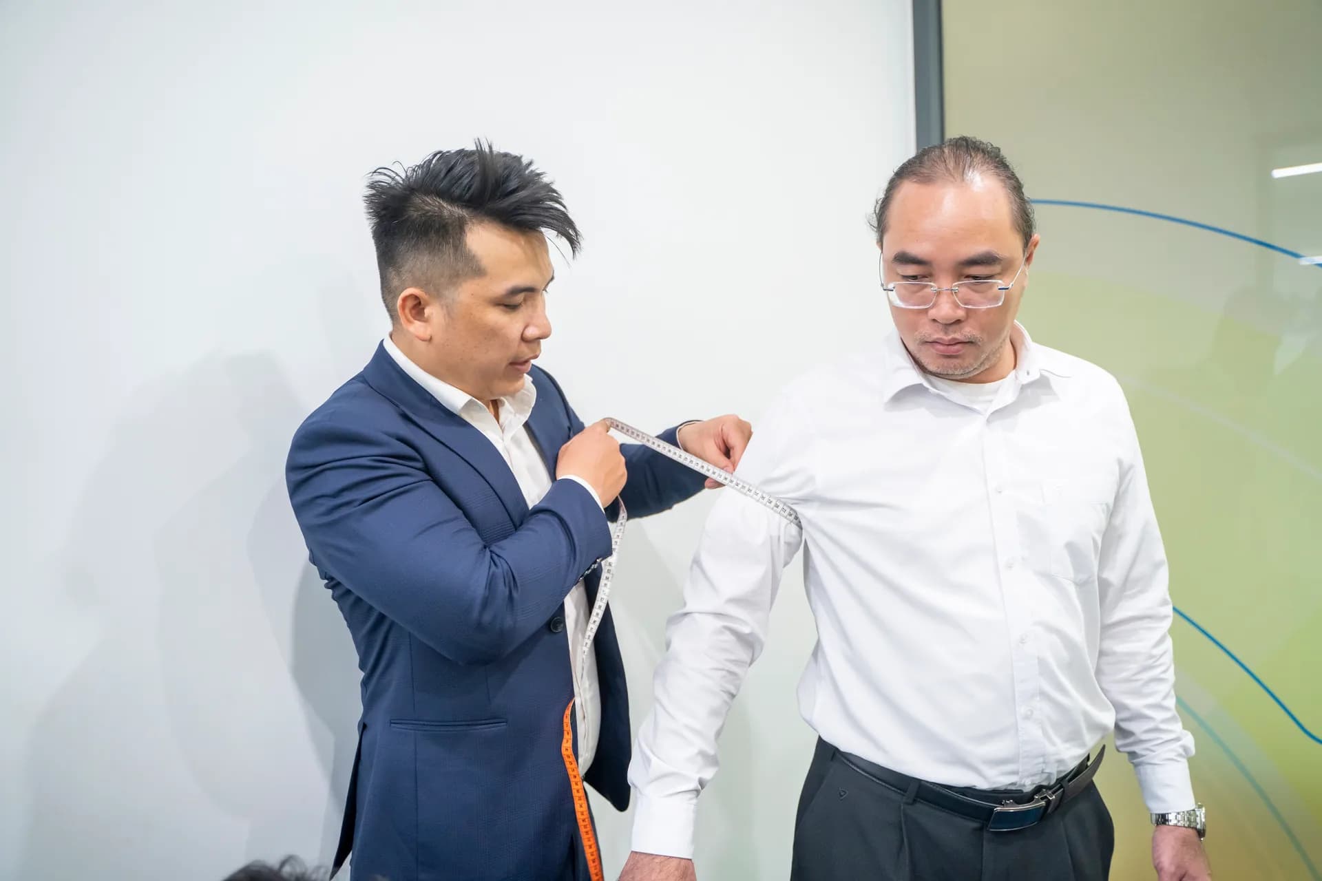 Chuyên viên Mon Amie đo tay áo cho nhân viên nam mặc sơ mi trắng, kiểm tra kỹ từng số đo của chiếc sơ mi trắng nam