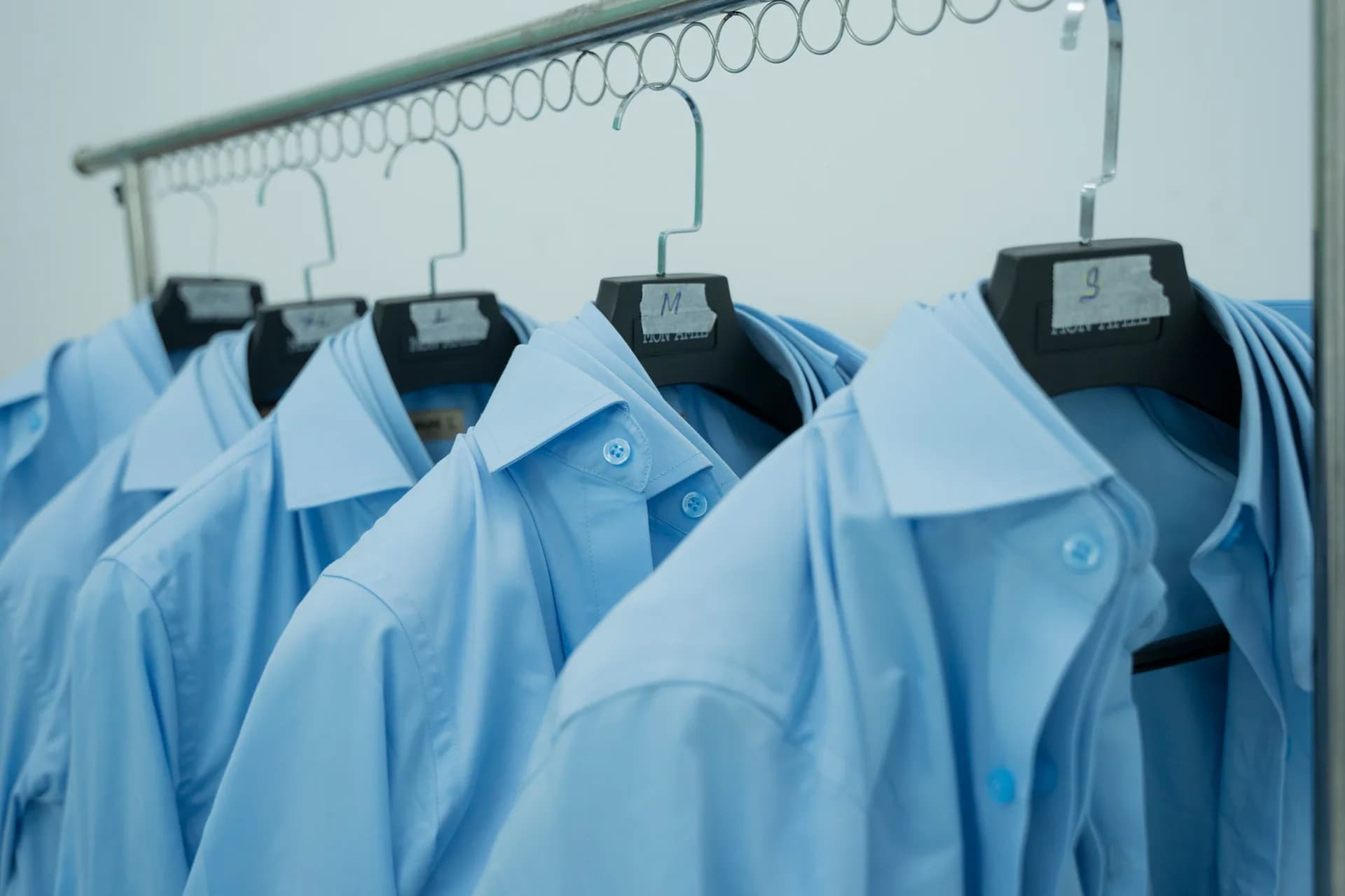 Áo sơ mi xanh mẫu gắn nhãn size S, M, L treo sẵn để nhân viên thử, minh hoạ đồng phục cho nhà hàng và sự kiện cao cấp