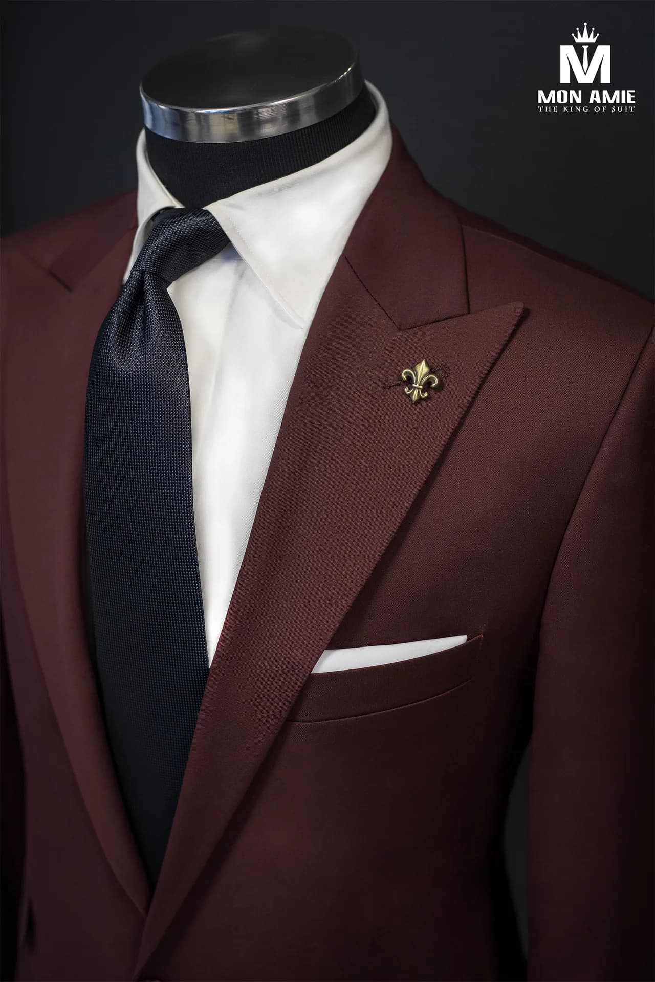 Cận cảnh ve áo suit đỏ đô, cà vạt navy và ghim cài hình hoa huệ, minh họa các chi tiết của bộ vest nam