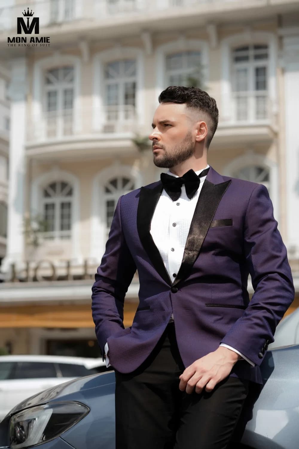 Tuxedo tím cận cảnh, ve satin đen và nơ bên xe hơi trước khách sạn cổ, minh họa bài hỏi gì trước khi chọn tiệm may vest