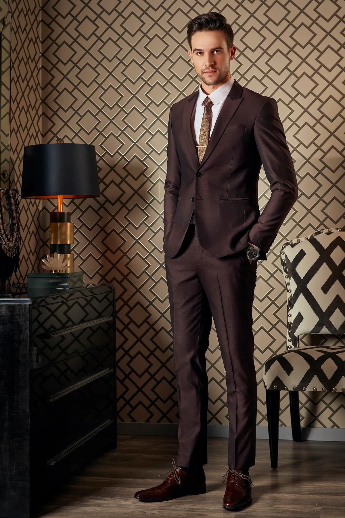 Suit nâu mocha ánh nhẹ, cà vạt ghim vàng trước nền họa tiết hình học, minh họa tiệm may vest quận 7 và Phú Mỹ Hưng