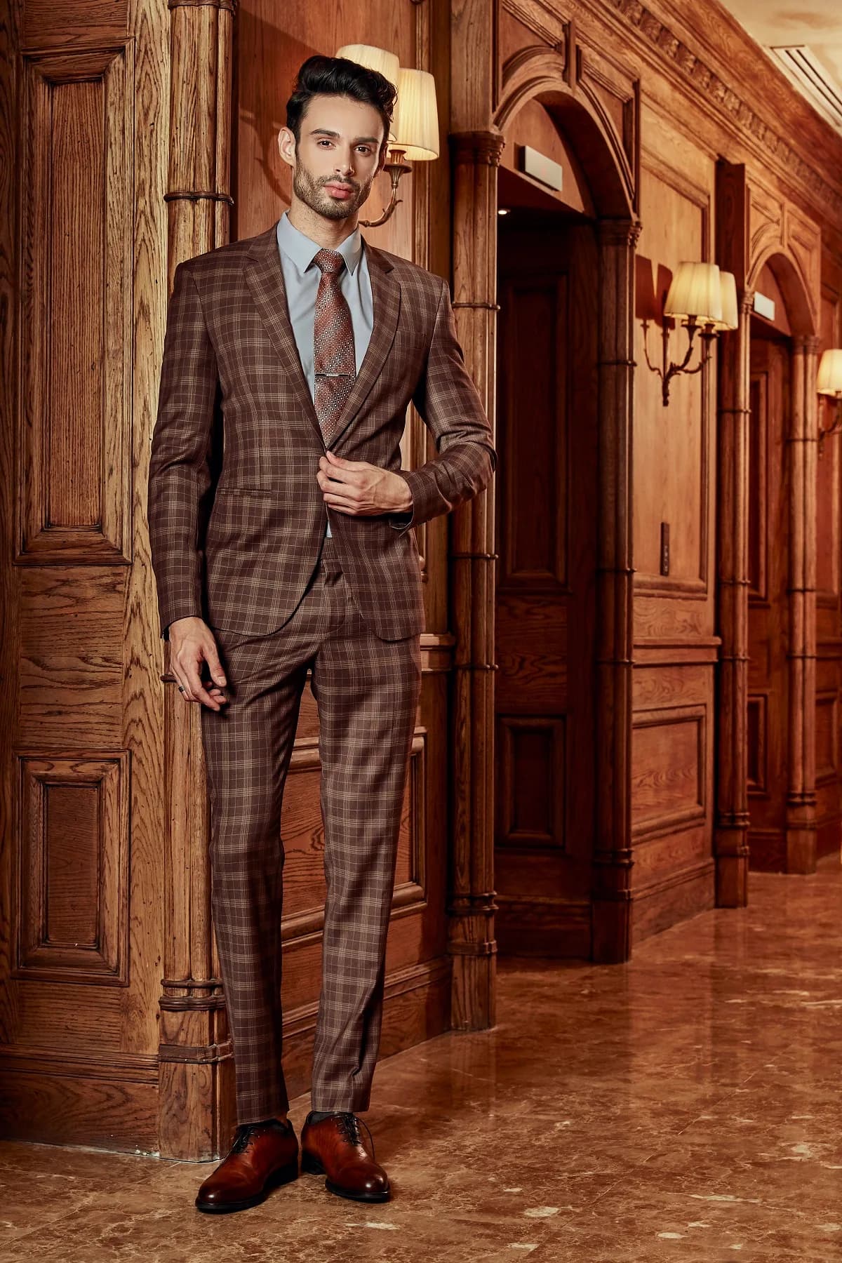 Suit ca-rô nâu socola, cà vạt đồng tông giữa hành lang gỗ, minh họa dịp nên có một bộ vest may đo