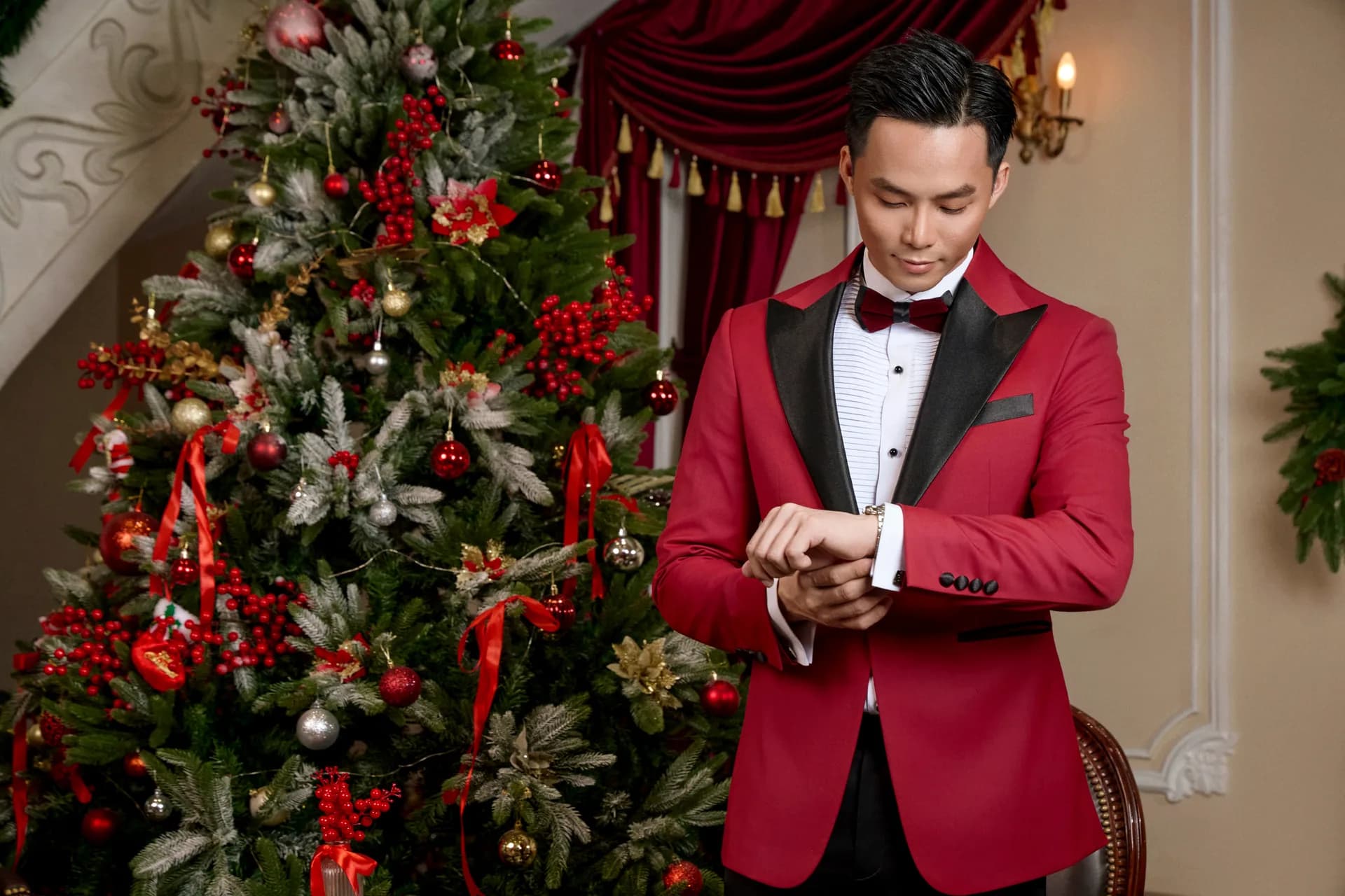 Cận cảnh tuxedo đỏ, ve satin đen, chỉnh cổ tay áo bên cây thông Noel, một chi tiết nhỏ khi mặc vest đúng cách