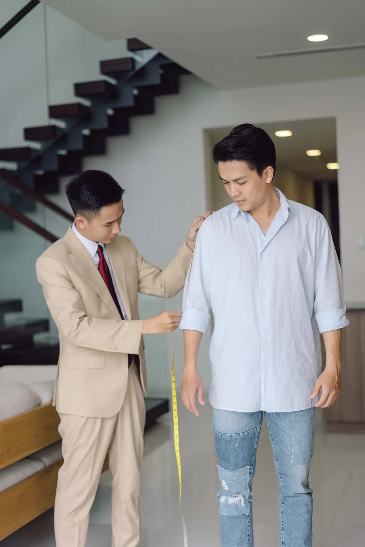 Đo tay áo trong ánh sáng dịu, thước dây vàng buông dọc thân, minh họa cách đo thông số áo vest