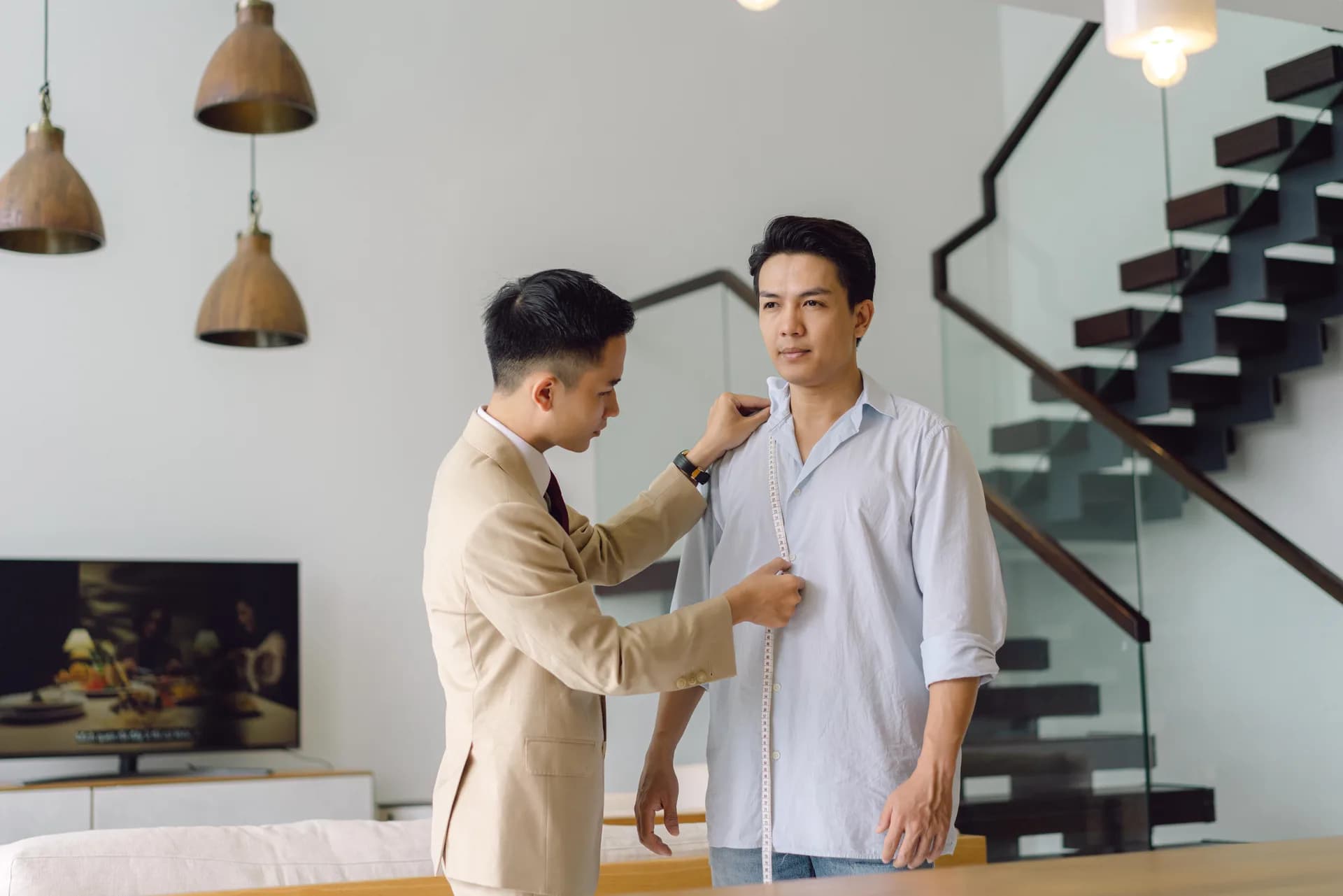 Nghệ nhân đo dài thân áo cho khách bên cầu thang kính, minh họa tiệm may vest Tân Bình và Gò Vấp