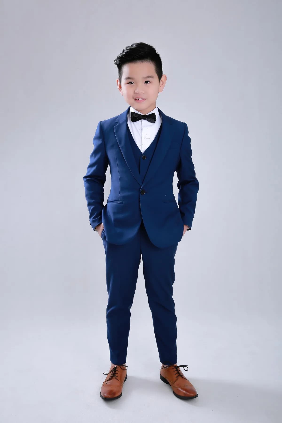 Bộ suit navy ba mảnh gọn gàng, giày da nâu, dáng đứng tự tin, minh họa cách người thấp mặc vest trông cao hơn