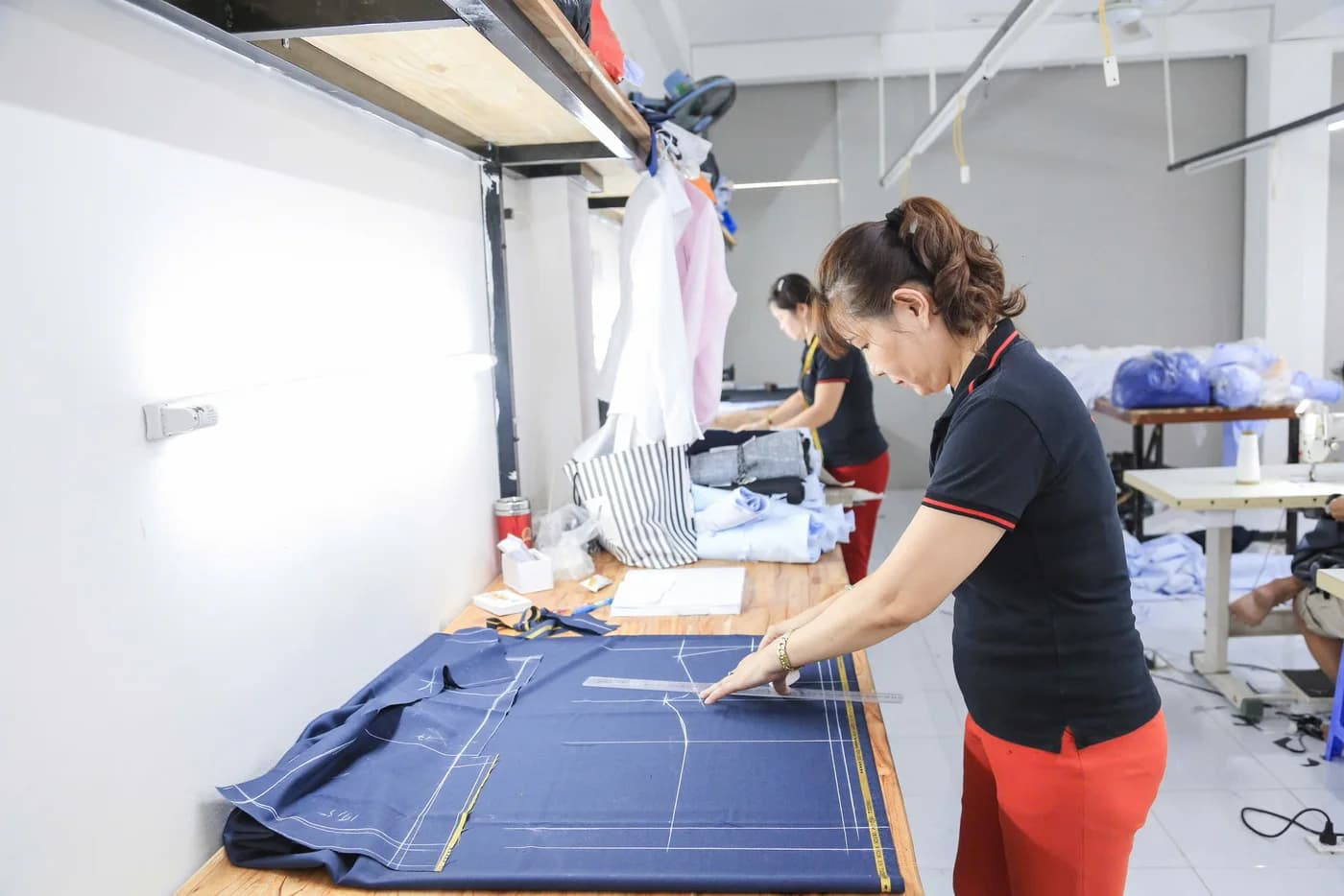 Thợ nữ áo đen quần đỏ kẻ rập trên vải xanh navy, minh hoạ nghề may vest tại các tiệm quận 1