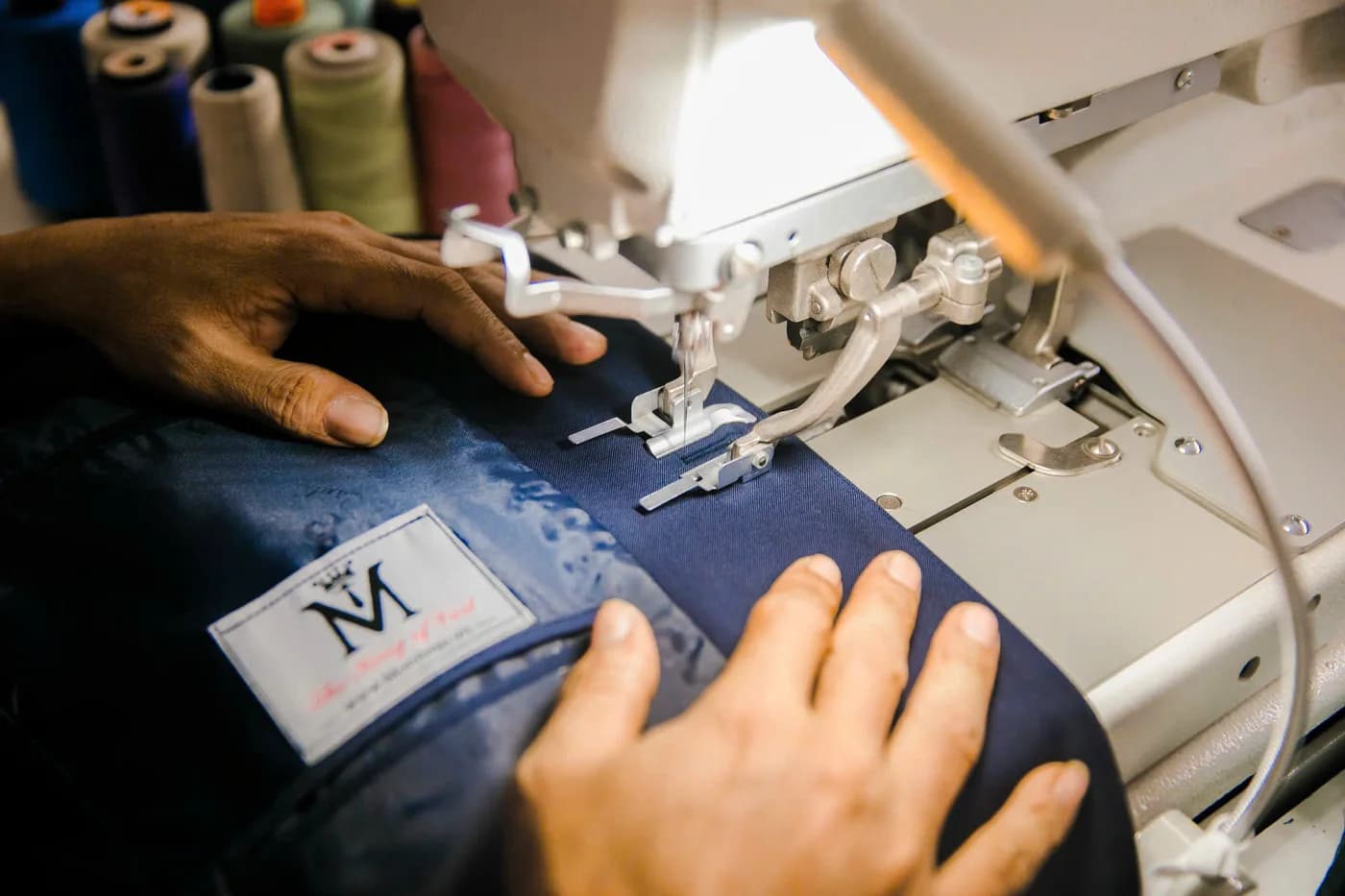 Cận cảnh bàn tay may thân vest xanh gắn nhãn Mon Amie, minh hoạ nghề may vest quận 3